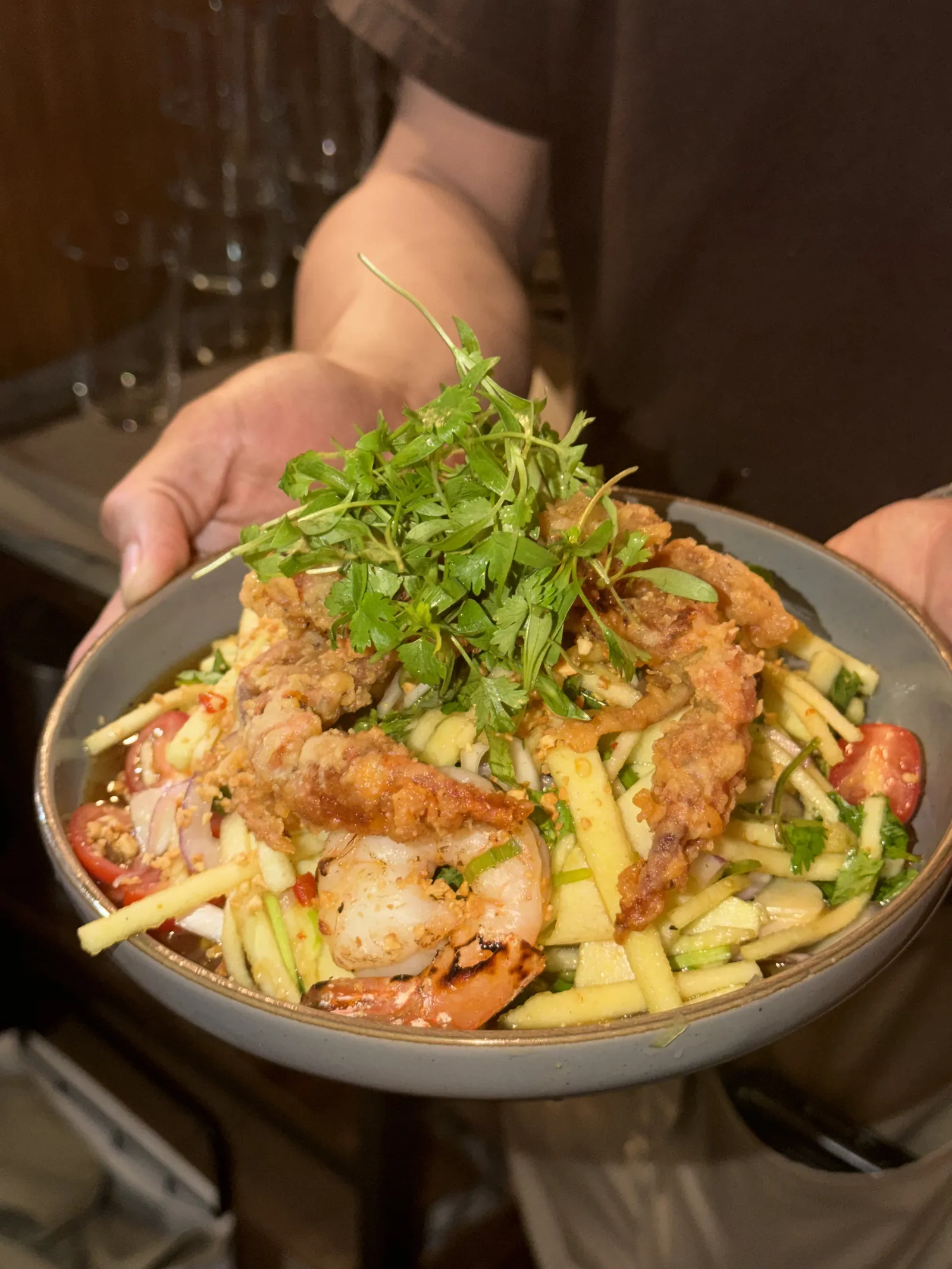 A server holding crispy soft-shell crab and prawns over a green apple salad